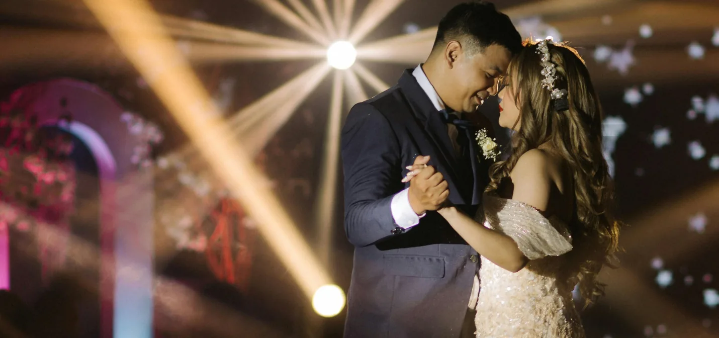 A couple sharing their first dance beneath warm beams of light