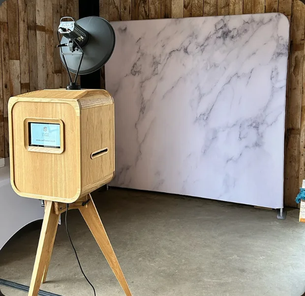 Wooden Rustic Pod on tripod legs beside a photo backdrop